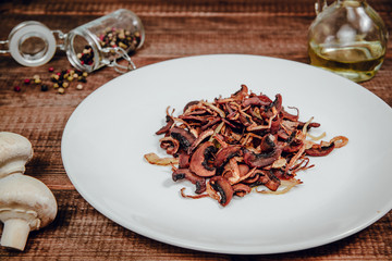 Fried Champignon on a wooden table. The concept of eating mushrooms, frying. Serving mushrooms with onions, side dishes. Tasty dishes.