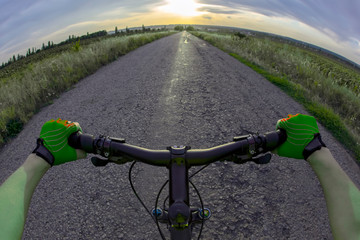 Obraz na płótnie Canvas hands on the steering wheel riding a cyclist on the road towards sunset