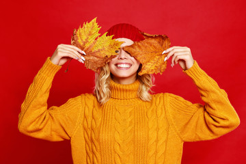 happy emotional cheerful girl laughing  with knitted autumn   cap and yellow sweater on colored red background.