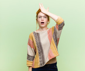 young pretty red head woman raising palm to forehead thinking oops, after making a stupid mistake...