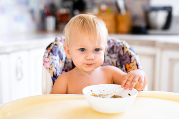 little baby at home sitting at the table and having meal