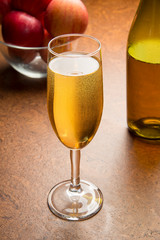 A glass of cold apple cider on a brown table with a glass bottle and ripe red apples. Selected focus.
