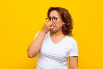 middle age woman feeling disgusted, holding nose to avoid smelling a foul and unpleasant stench...