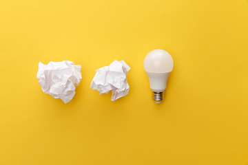 top view of crumpled paper near light bulb on yellow background