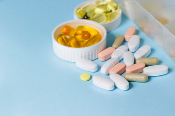 Capsules and tablets of drugs in containers and on the table on a blue background.