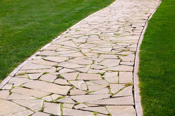 flagstone footpath in a park with a green lawn goes into perspective on a sunny summer day,...