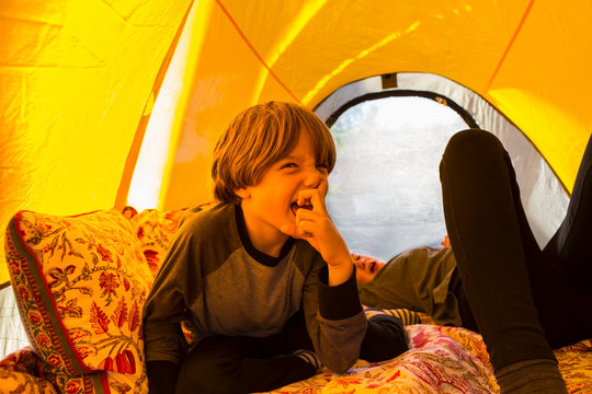 6 year old boy playing inside tent sticking finger in nose