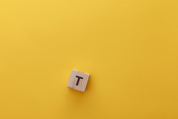top view of wooden cube with t letter on yellow background
