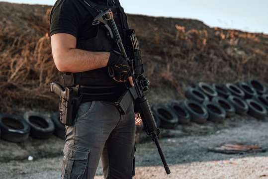 Image of armed man with rifle and gun standing outdoors, close-up.