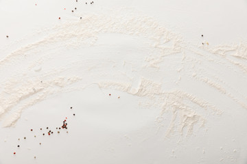 top view of white surface with scattered peppercorns and flour