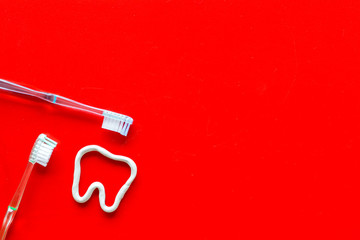 Teeth brushing concept. Tooth drawn with toothpaste near toothbrushes on red background top view copy space