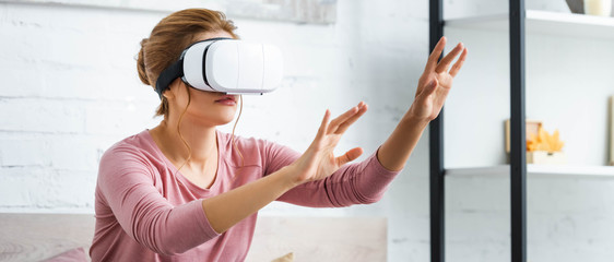 panoramic shot of young adult woman playing with virtual reality headset in apartment
