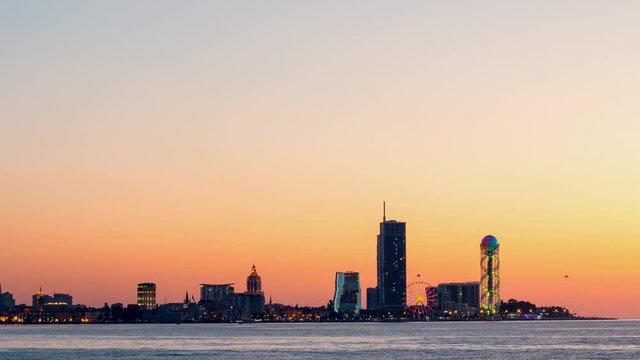 Amazing timelapse of Batumi city skyline with beautiful orange sky in sunset time. Modern architecture In seafront promenade with evening illuminations lights.