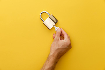 cropped view of man holding key in padlock on yellow background