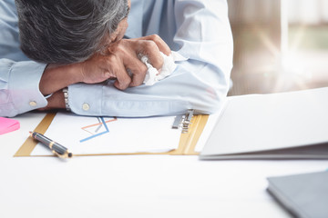 The businessman sat down at the desk in the office with a tissue on hand after the stock market sale report failure. He was tired, crying and frustrated. Business concept. Overworked and Sleeping.