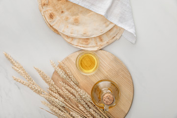 top view of lavash bread covered with white towel near cutting board with spikes and oil on marble surface