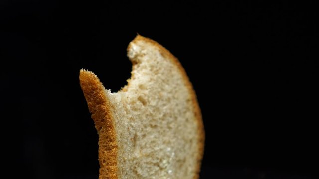 Bitten slice of the toast bread rotates, isolated over the white background