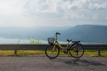 Fototapeta premium Active life / A young man with a bike enjoys the sky view on top of mountain. A young man is cycling into the sunset in the park. Young man relax with beautiful landscape image and Bicycle.