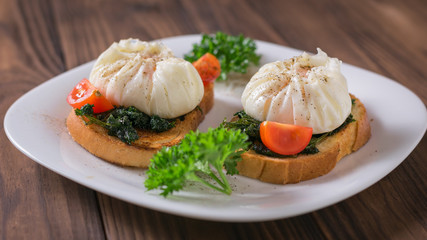 Cherry tomatoes with poached eggs on pieces of bread on a wooden table.