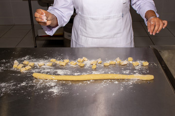Chef making a potato gnocchi pasta. Showing only his hands, on a stainless steel floured worktop. Your hands are dirty with flour.
