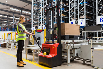 Storehouse employee in uniform working on forklift in modern automatic warehouse.Boxes are on the...