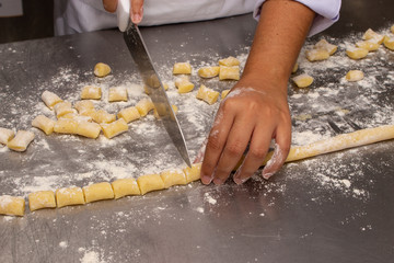 Chef making a potato gnocchi pasta. Showing only his hands, on a stainless steel floured worktop....