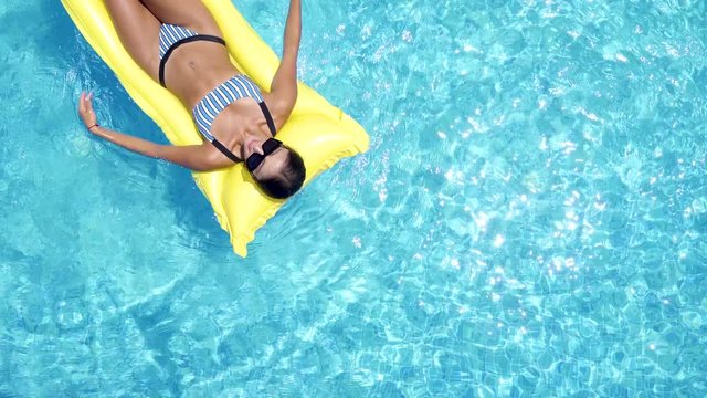 Close up top view of girl in bikini on inflatable yellow mattress sunbathing travel holidays at resort pool. Young sexy girl relaxing in blue swimming pool in sunny day. 4K