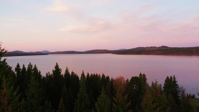 Aerial view of sunrise over lake Zuratkul; picturesque colours of morning sun in countryside; sunbeams over forest; silhouette of pine tree in morning shadow; amazing autumn sky, pink, purple colors