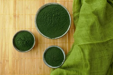Obraz na płótnie Canvas Spirulina seaweed. Spirulina powder in cups set and green scarf on bamboo mat background.Healthy food.