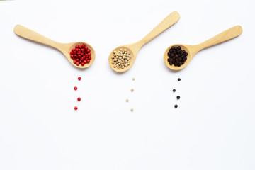 Red, white and black peppercorns with wooden spoon on white