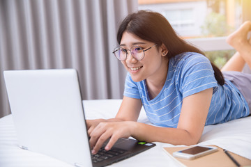 Girl teen nerdy happy smile working homework or chat with friends by laptop on the bed weekend day.