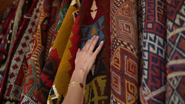 Close up of hands feeling Turkish rugs hanging from a display rack outside in Cappadocia