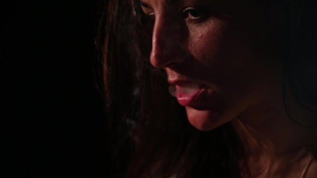 The brunette smokes an electronic cigarette on a black background, releases thick smoke from her mouth. Portrait of a woman smoking a vape, hovering.