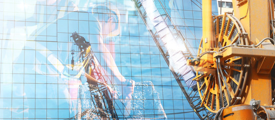 Lift cranes is reflected from the mirror of the building.Double exposure.Construction workers are working.