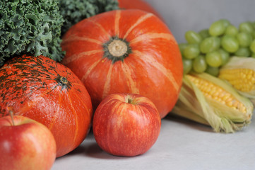 Pumpkins, corn on the cob, cale salad, grapes, apples. Autumn harvest concept - fruits and vegetables. Close-up. Light background. 