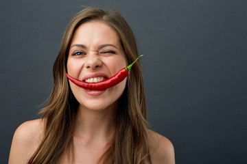woman with naked shoulders and long hair  biting red hot chilli peppers.