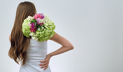 Woman standing back holding flowers on shoulder.
