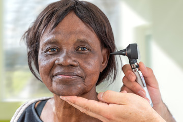 Doctor holding otoscope and examining ear of senior African woman.