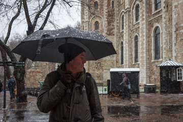 Adult man with black umbrella under a snowfall in the Tower of London.