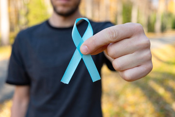 Man hands hold blue Prostate cancer awareness ribbon against the background of the autumn forest. Medicine and healthcare concept, Men's health.