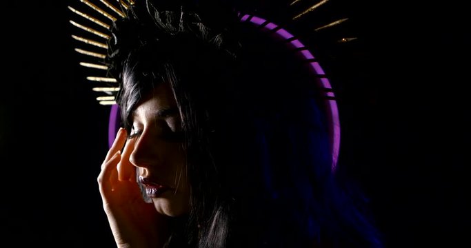 tender young brunette with fashion halo spiked headdress is posing in dark studio with neon lights