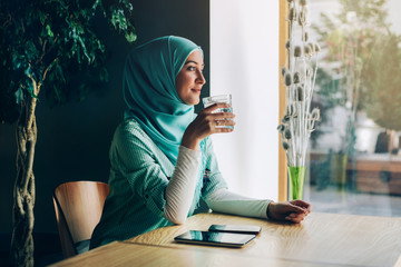 Beautiful young arabic girl in hijab posing for camera at cafe.