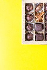 Assortment of sweet confectionery with chocolate candies and pralines in a gift box on a yellow paper background. Top view. 
