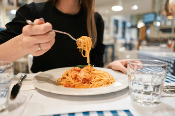 Close-up spaghetti Bolognese wind it around a fork. Parmesan cheese. Young woman eats Italian pasta...