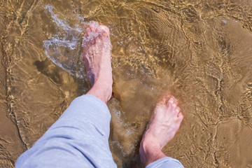 Man's barefooted feet on trousers. Man is walking on water shallow on sand bottom, legs close up. Enjoying summer vacation.