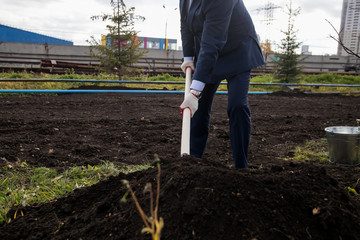 man in a business suit with a shovel plant a new tree