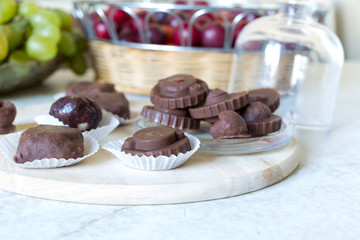Homemade raw chocolate sweet candies with raspberries inside lay on round kitchen board on white table with fruits in basket in background.