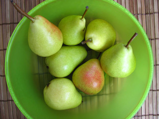Seven fresh pears in a green translucent bowl on a wooden table. Autumn harvest of fruits. Flat lay, top view.