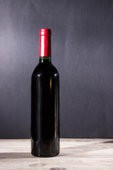 Wine bottle standing on a wooden table with a dark background.