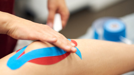 Obraz na płótnie Canvas Sports injury kinesio treatment. therapist placing kinesio tape on patient's knee